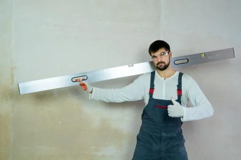 Caucasian builder with construction ruler shows thumb up in interior free space Stock Photos