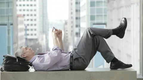 Caucasian businessman laughing while laying on a bench text messaging on cell Stock Footage