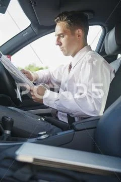 Caucasian Businessman Reading Paperwork In Car