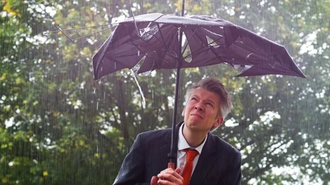 Caucasian businessman sheltering underneath a broken umbrella in the rain Stock Footage 80923715