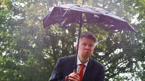 Caucasian businessman sheltering underneath a broken umbrella in the rain 스톡 동영상 80924375