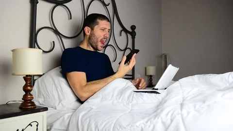 Caucasian businessman working while on bed he's angry and screams on smartphone 스톡 동영상 122306351