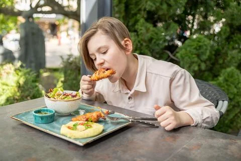 Caucasian child in cafe eats chicken skewers with appetite. Teen boy has br.. Stock Photos