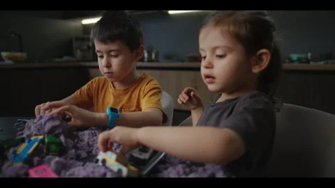 Caucasian children playing with multi-colored polymer sand at home table Stock Footage 270426932