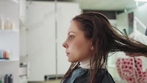 Caucasian client sits while stylist pulls and detangles wet hair to distribute Vídeo Stock 321653121