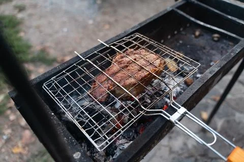 Caucasian close-up hands cooking beef steak on the grill net on coal bbq Stock Photos