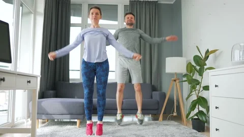 Caucasian couple is doing jumping jacks exercise at home in cozy bright room. Stock Footage 154260779