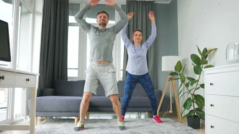 Caucasian couple is doing jumping jacks exercise at home in cozy bright room. Video stock 155093814