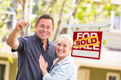 Caucasian Couple in Front of Sold Real Estate Sign and House with Keys Stock Photos