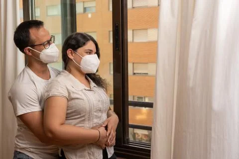 Caucasian couple hugging while looking outside of window wearing mask Stock Photos