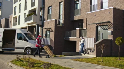 Caucasian courier in face mask carry parcel boxes on a trolley from a van and Stock Footage 166350641