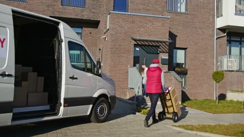 Caucasian courier in red uniform carry parcel boxes on a trolley from a van and Stock Footage 166350510