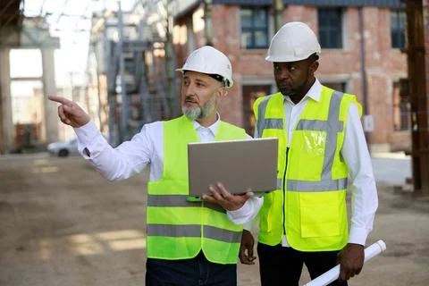 Caucasian elderly builder with wireless laptop explaining all peculiarities of Stock Photos