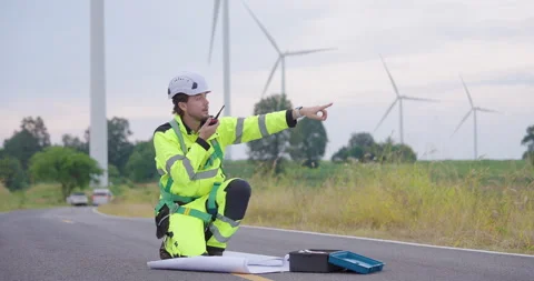 Caucasian engineer kneeling on rural road beside blueprint plan, using walkie Stock Footage 337166323