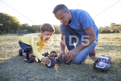 Caucasian Father And Son Playing With Remote Control Cars In Field
