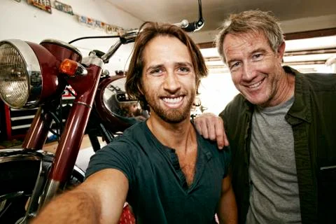 Caucasian father and son posing for selfie with motorcycle in garage Stock Photos