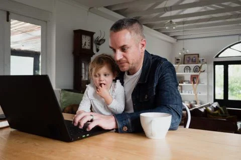 Caucasian father getting work done on laptop while daughter sitting on his lap Stock Photos