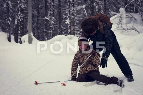 Caucasian Father Helping Cross-Country Skiing Daughter Falling In Snow