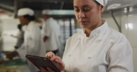 Caucasian female chef using tablet in restaurant kitchen with other chefs in Stock Footage 149540005