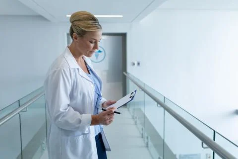 Caucasian female doctor standing in hospital corridor looking at medical chart Stock Photos