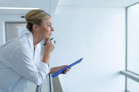 Caucasian female doctor standing in hospital corridor holding medical chart Stock Photos