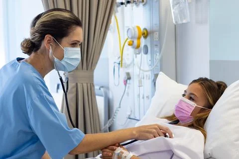 Caucasian female doctor using stethoscope on girl patient lying in hospital.. Фото