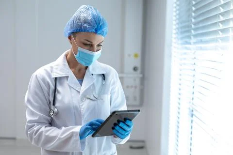 Caucasian female doctor wearing mask and latex gloves using tablet Stock Photos