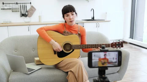 Caucasian female recording guitar tutorial at home with laptop and camera Stock Footage 291036968
