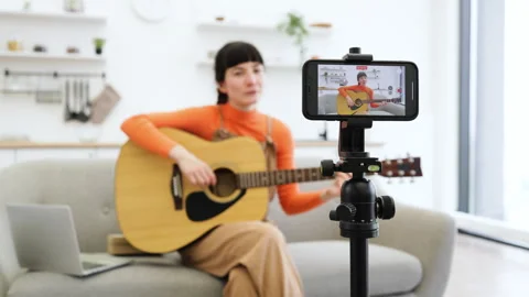 Caucasian female recording guitar tutorial at home on smartphone 스톡 동영상 291256425