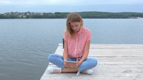Caucasian female watching at tablet while sitting near lake Stock Footage 91726212