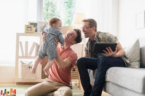 Caucasian gay fathers and baby relaxing in living room Stock Photos