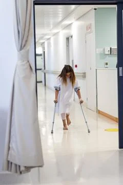 Caucasian girl patient with head down walking with crutches in hospital cor.. Stock Photos