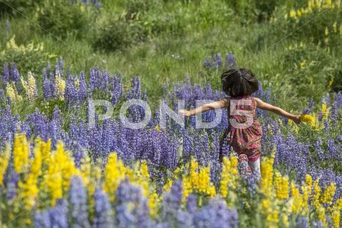 Caucasian girl running on hillside with wildflowers Stock Photos