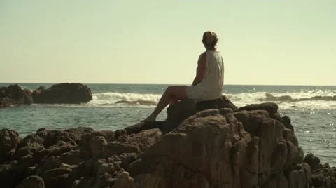 Caucasian girl sitting on the rocks watching the ocean Stock Footage 45989853