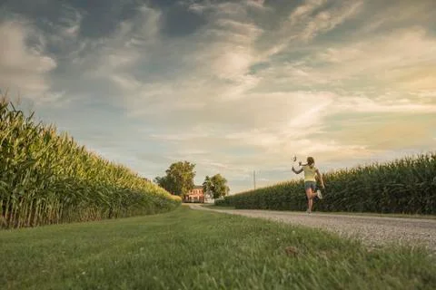 Caucasian girl walking on dirt path by corn field Stock Photos