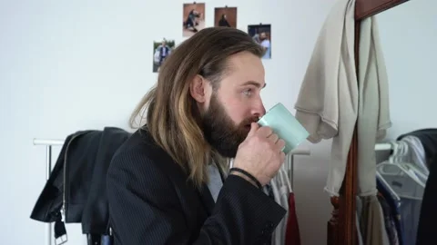 Caucasian good-looking guy in a suit  is looking in a mirror drinking coffee Stock Footage 147897200