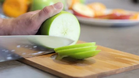 Caucasian guy cuts a green apple a metal knife on a wooden board. Round slices. Stock Footage 112939546