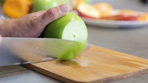 Caucasian guy cuts a green apple a metal knife on a wooden board. Round slices. Stock Footage 113349070