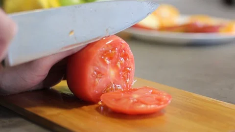 Caucasian guy cuts a red tomato a metal knife on a wooden board. Round slices. Stock Footage 112939544