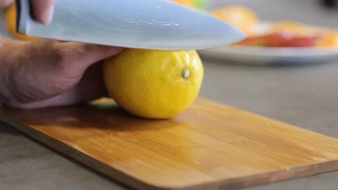Caucasian guy cuts a yellow lemon a metal knife on a wooden board. Round slices. Stock Footage 113349079
