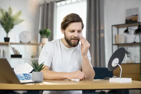 Caucasian guy performs hygienic procedures, cleaning his face with cotton pad Stock Photos