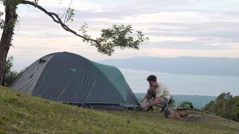 Caucasian guy setting up tent in the mountain hill with spectacular natural view Stock Footage 116355397