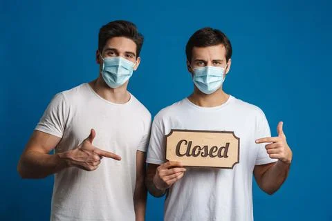 Caucasian guys in masks gesturing while showing closed sign board Stock Photos