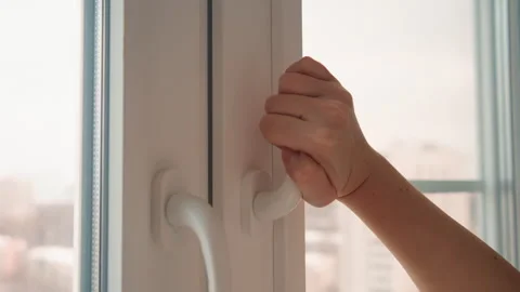Caucasian hand gently tilts window for fresh air. Peaceful scene depicted with Stock Footage 346233437