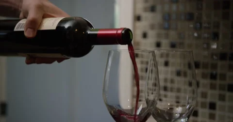 Caucasian hand pours two large glasses of red wine. Slow motion. Stock Footage 64025533
