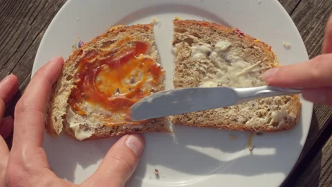 Caucasian hand spreading orange-colored jam on a bread with butter on it Stock Footage 199626770