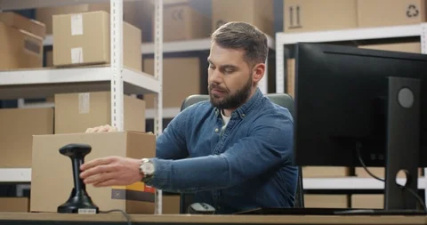 Caucasian handsome mailman working at computer in post office store with parcels Stock Footage 126473771