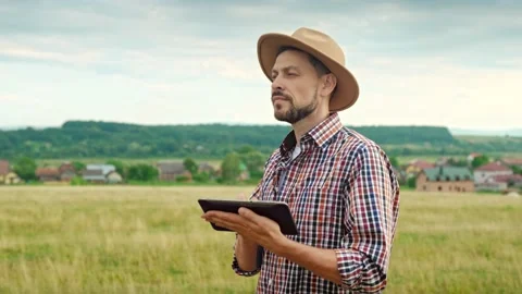 Caucasian handsome man in hat standing in grassland and using tablet device Stock Footage 205503553