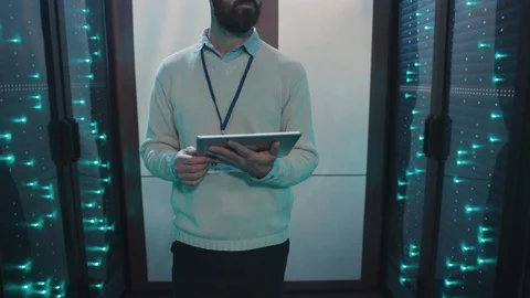 Caucasian IT administrator walking in server rack corridor running diagnostics Stock Footage 119231723