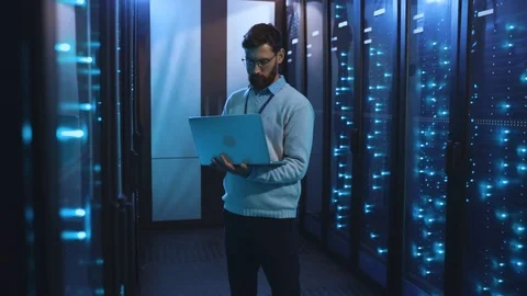 Caucasian IT engineer in high tech server room using modern laptop checking Видео 118450032